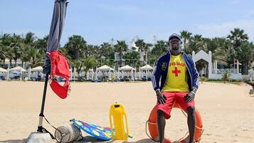 A lifeguard on a sandy beach with beach umbrellas and palm trees in the background.