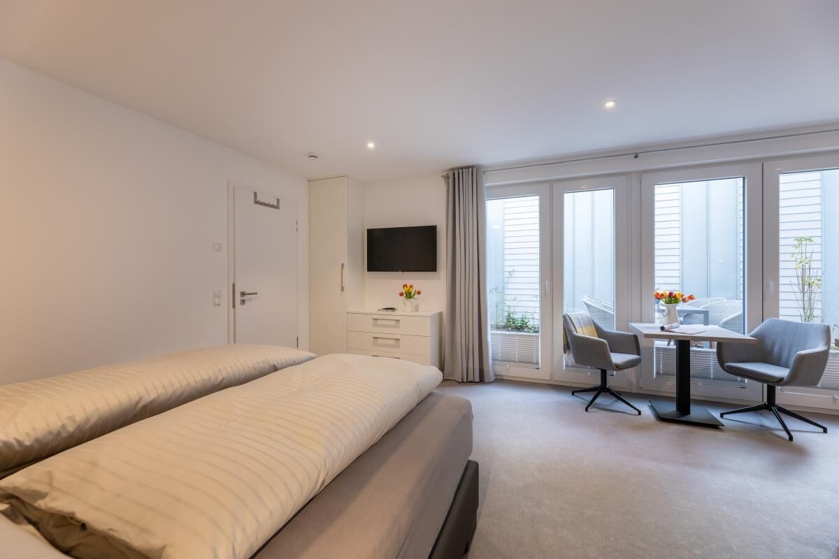 Ett hotellrum med en säng, en TV, ett skrivbord med två stolar och ett fönster med persienner.