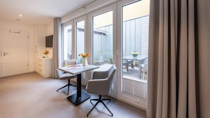 Una habitació moderna amb un gran finestral, una taula de treball amb dues cadires i una taula petita amb flors.