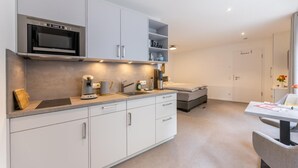 Una cuina moderna amb armaris blancs, microones integrat i cafetera.