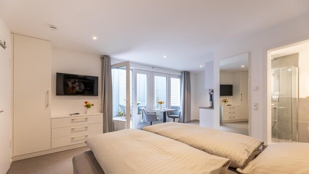 Habitació d'hotel moderna amb un llit gran, televisió, escriptori amb cadira i un balcó amb taula i cadires.