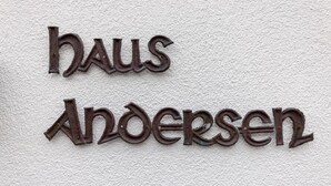 Ein Metallschild mit der Aufschrift "haus Andersen" an einer strukturierten Wand befestigt.