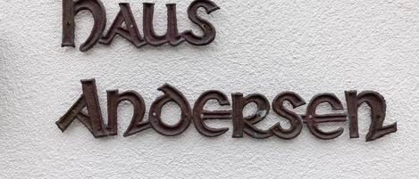 A metal sign with the words 'haus Andersen' mounted on a textured wall.