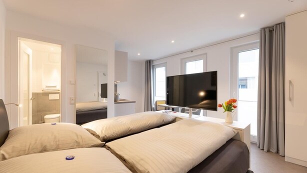 Ein modernes Hotelzimmer mit einem großen Bett, einem Flachbildfernseher und einem durch eine offene Tür einsehbarer Badezimmer.