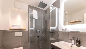 Ein modernes Badezimmer mit einer gläsernen Duschkabine, einer weißen Toilette und einem Waschtisch mit Spiegel.