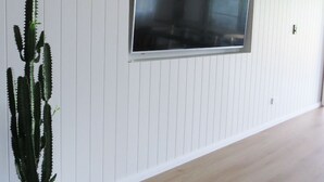 Une pièce dotée d’une grande fenêtre, de murs recouverts de panneaux blancs, d’un plancher en bois et d’un cactus en pot.