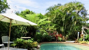Une piscine aux eaux cristallines, dotée d’une terrasse en bois et d’un parasol blanc.