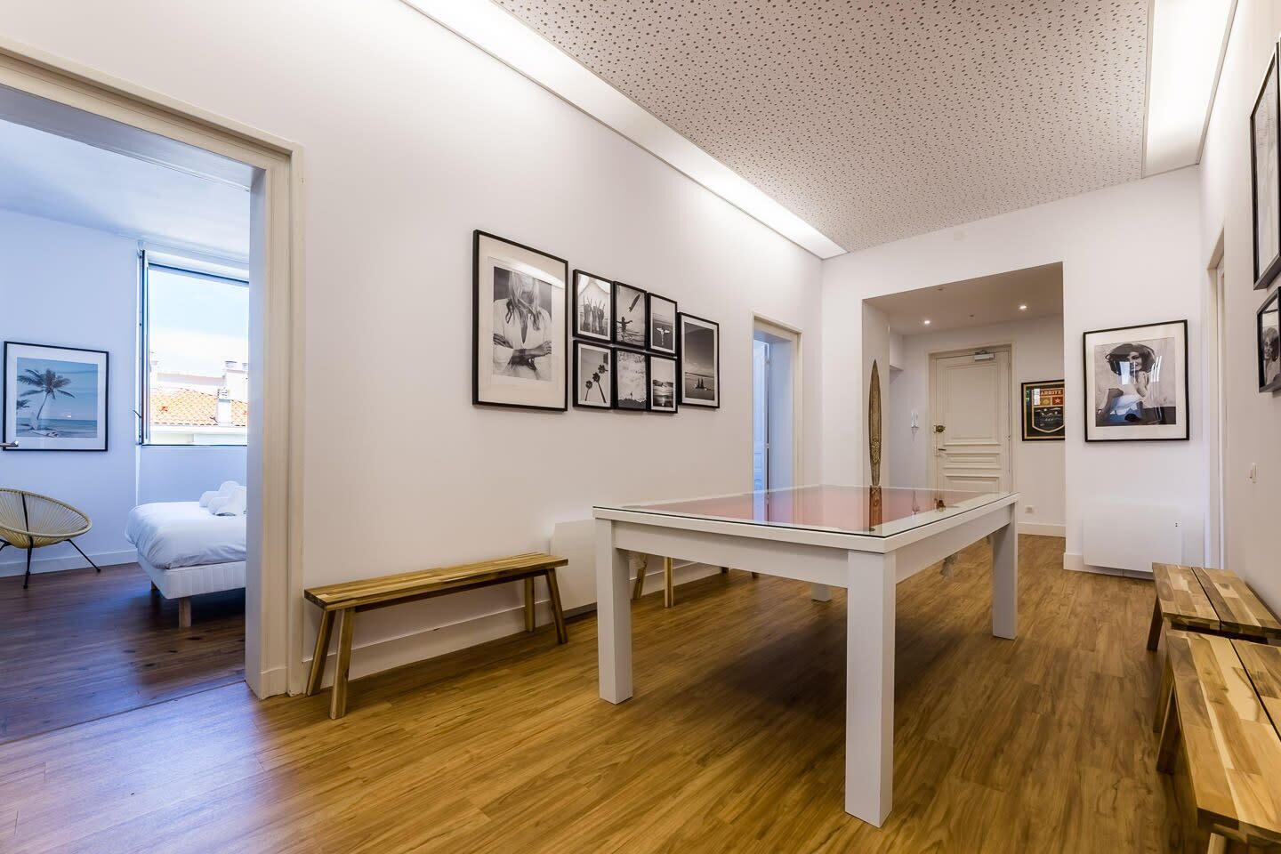 A modern art gallery with a white table, framed pictures on the walls, and wooden flooring.