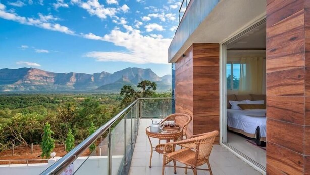 A balcony with wicker furniture, a bed, and a view of mountains. - Stay Serene Luxury  (Murbad)