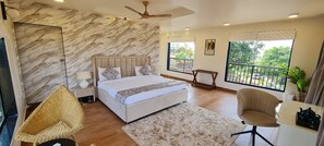 Un dormitorio moderno con pared de mármol, cama con cabecero, balcón con barandilla y vistas al verdor exterior.
