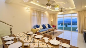 A modern living room with a dining area, large windows, and a view of the outdoors. - Stay Serene Luxury  (Murbad)