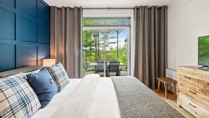 A bedroom with a large bed, a dresser, a TV, and a view of the outdoors. - Tremblant Prestige - Les Eaux 235-1 (Mont-Tremblant)
