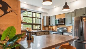 A modern kitchen with a large island, stainless steel appliances, and pendant lighting. - Tremblant Prestige - Les Eaux 235-1 (Mont-Tremblant)