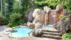 A naturalistic pool area with a waterfall, surrounded by rocks and greenery. - Tremblant Prestige - Les Eaux 235-1 (Mont-Tremblant)