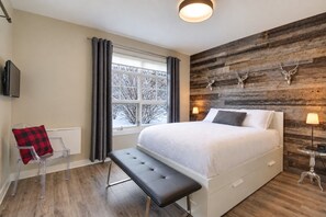 A bedroom with a large bed, a bench, a TV, and a wooden wall with antlers.