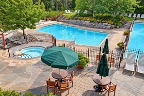 Une piscine avec un jacuzzi, entourée de carreaux de pierre, et aménagée avec des meubles de jardin et des parasols.