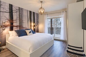 A bedroom with a large bed, a view of the outdoors through a window, and a chandelier.