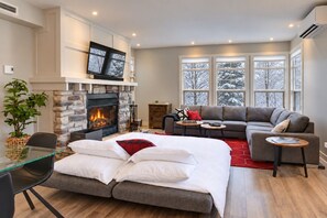 A modern living room with a fireplace, a sofa, a dining table, and a TV mounted on the wall.