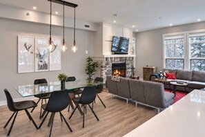 Un salon moderne avec une cheminée, un coin repas doté d’une table en verre et un canapé.