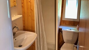 Ein Badezimmer mit Holzvertäfelung, einer Duschkabine mit Vorhang, einem Waschbecken und einer Toilette.