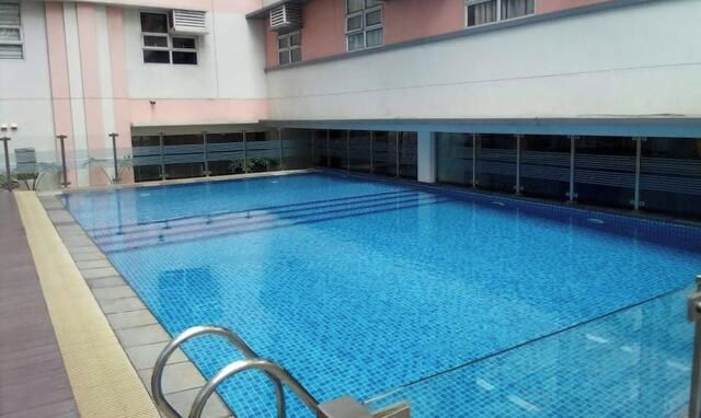 An indoor swimming pool with clear blue water, surrounded by a building with pink and grey walls and multiple windows.
