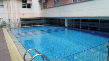 An indoor swimming pool with clear blue water, surrounded by a building with pink and grey walls and multiple windows.
