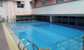 Piscina interior com água azul cristalina, rodeada por um edifício com paredes rosa e cinzentas e várias janelas.