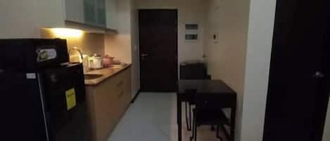 A narrow hallway with a kitchen area on the left, a dining table in the center, and a door on the right.