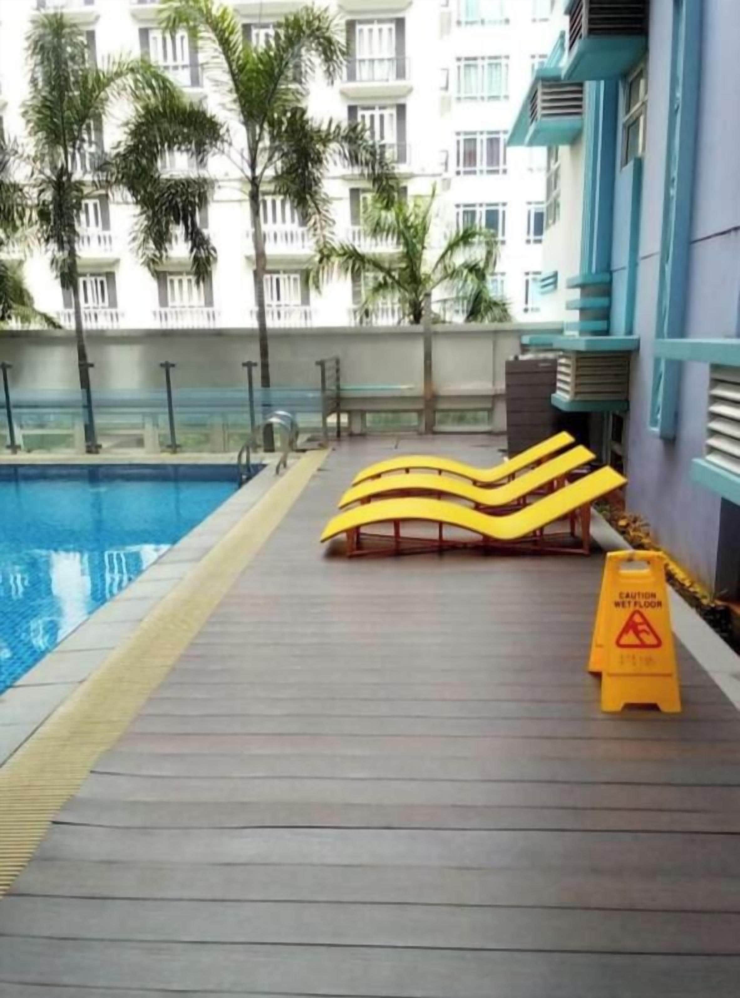 A swimming pool area with a wooden deck, yellow loungers, and a caution sign.
