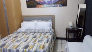A hotel room with a bed, a nightstand, a lamp, and a painting of mountains on the wall. - 101 Newport Boulevard all inclusive rate (Pasay)