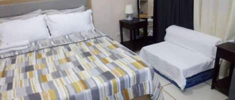 Habitación de hotel con una cama, una cama o sofá adicional, una mesita de noche con lámpara y un espejo.