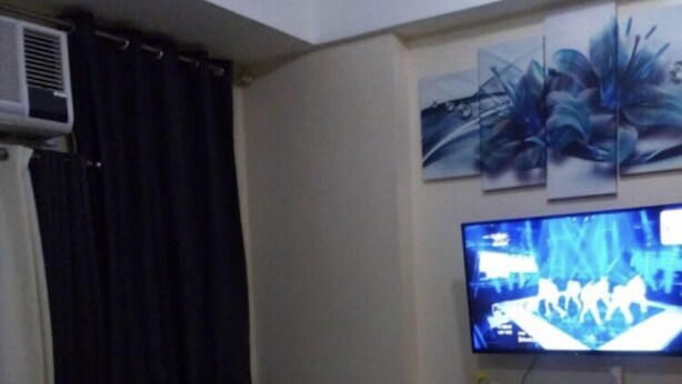 A living room with a dark-colored sofa, a flat-screen TV mounted on the wall, and a small table with a flower vase. - 101 Newport Boulevard all inclusive rate (Pasay)