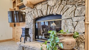 A stone fireplace with a flat-screen TV above it, a wooden cabinet below, and a potted plant to the right.