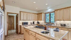 A spacious kitchen with granite countertops, wooden cabinets, a stainless steel sink, and a large window providing natural light.