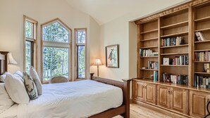 A bedroom with a large bed, wooden bookshelves, and large windows.