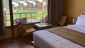 A bedroom with a large bed, a wooden desk, a chair, and a view of the hotel courtyard. -  Pangong Retreat Camp (Leh)
