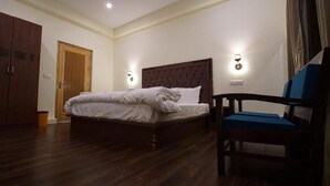 A bedroom with a large bed, a wooden wardrobe, a chair, and two wall-mounted lights. - Gopa Residency Temisgam Village  (Leh)