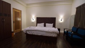 A bedroom with a large bed, two bedside tables, a wardrobe, and a chair. - Gopa Residency Temisgam Village  (Leh)