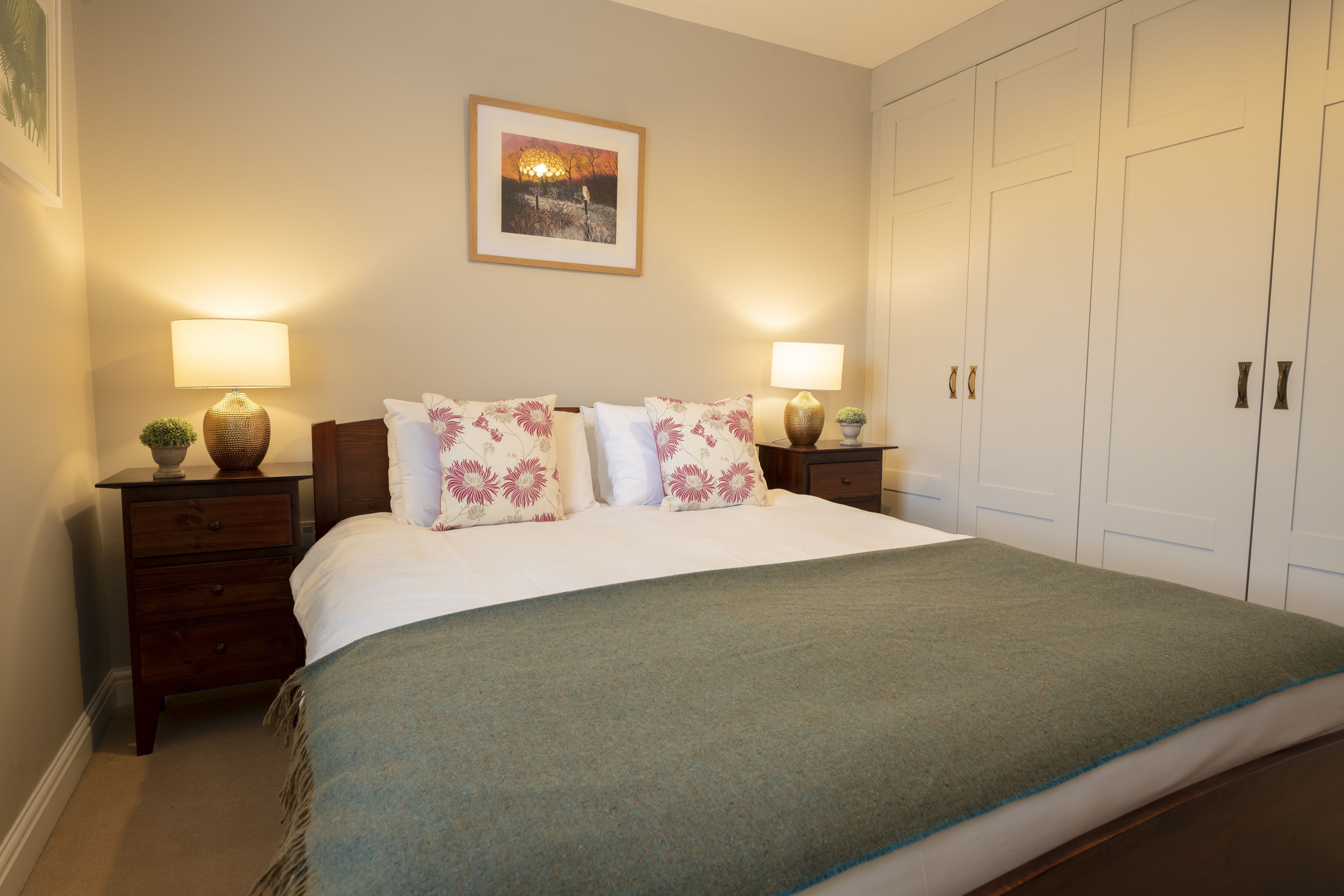 A neatly made bed with floral pillows, two bedside lamps, and a framed picture on the wall.
