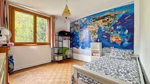 Habitación infantil con un mural de un mapa del mundo, una cama, una estantería y una ventana con cortinas.