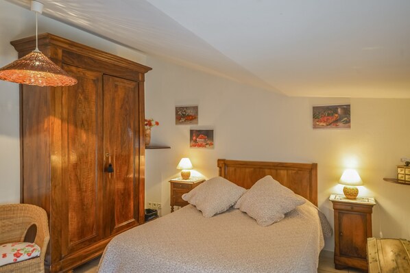 A bedroom with a wooden wardrobe, a bed with two pillows, two bedside lamps, and a hanging light fixture.