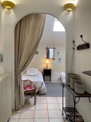 A bedroom with a bed, a chair, a bedside table with a lamp, a mirror, and a shelf with baskets.