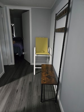 A room with a wooden floor, a white chair, a small table, a yellow screen, and a metal rack against the wall.