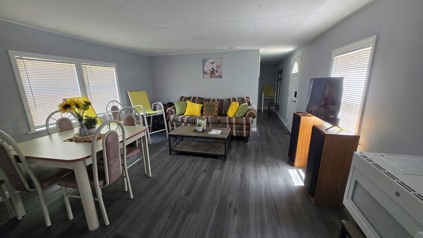 Uma sala de estar com uma mesa de jantar, cadeiras, um sofá, uma mesa de centro e uma televisão.