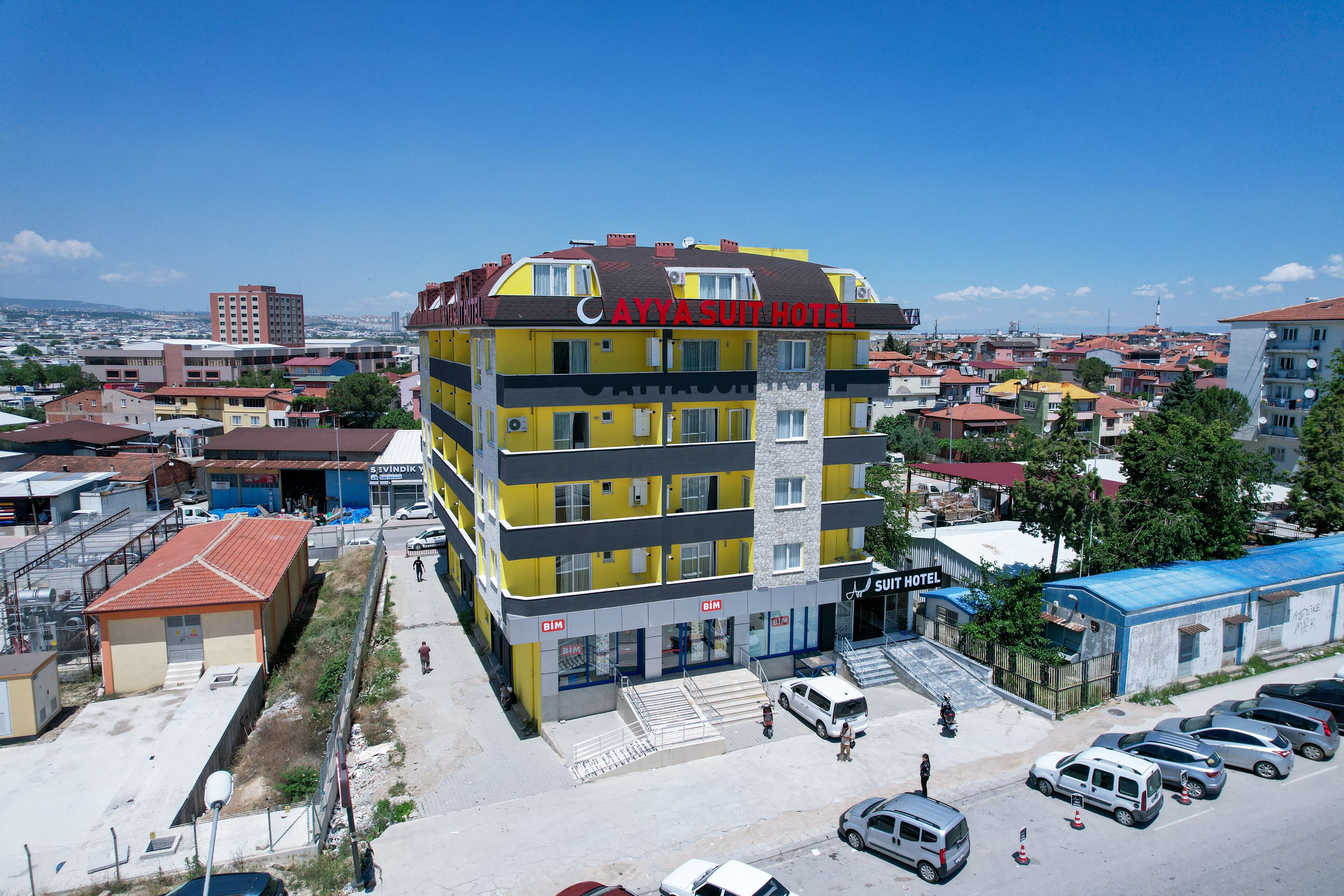 A multi-story hotel with a yellow facade and a red roof, featuring a prominent sign for the "CAYYA SUIT HOTEL".