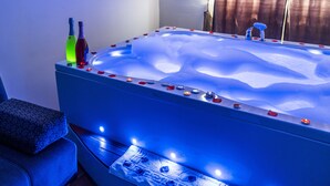 Un jacuzzi grande e iluminado con pétalos de rosa y velas, un sofá azul y un cojín estampado.