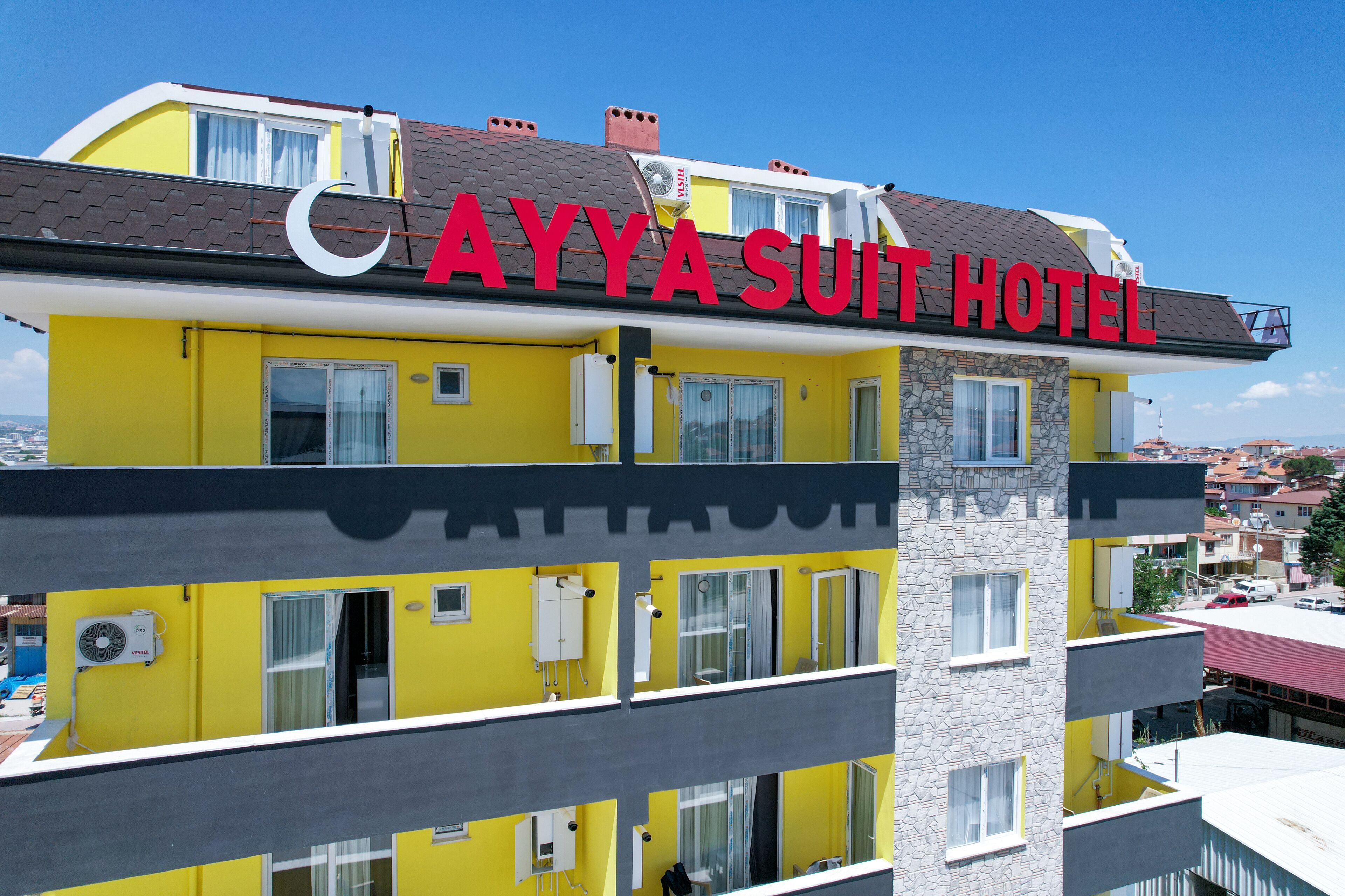 Un immeuble à plusieurs étages, doté d’une façade jaune vif et d’une enseigne indiquant « AYYA SUIT HOTEL ».