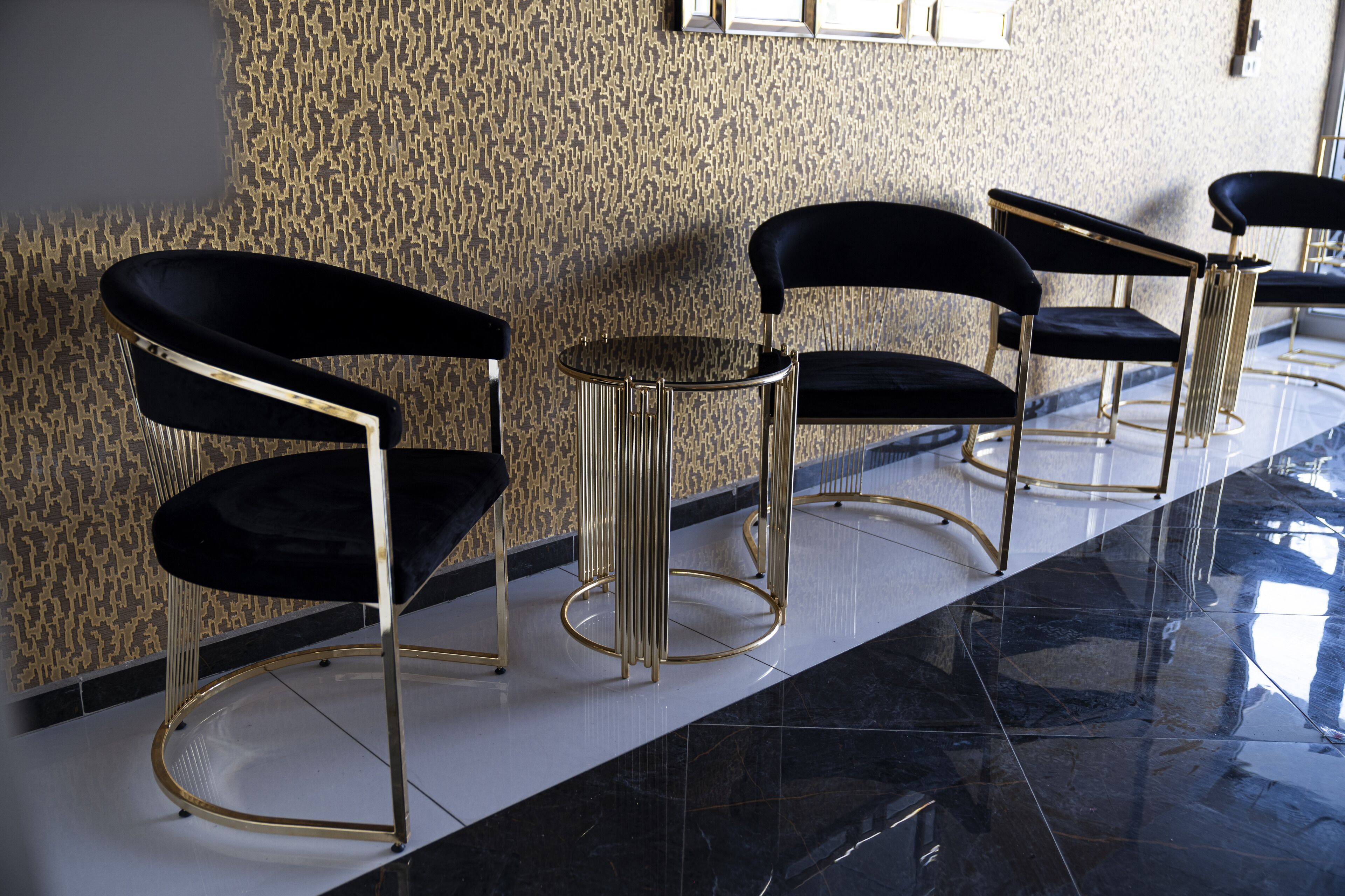 A row of black chairs with gold accents, a small round table, and a patterned wall.
