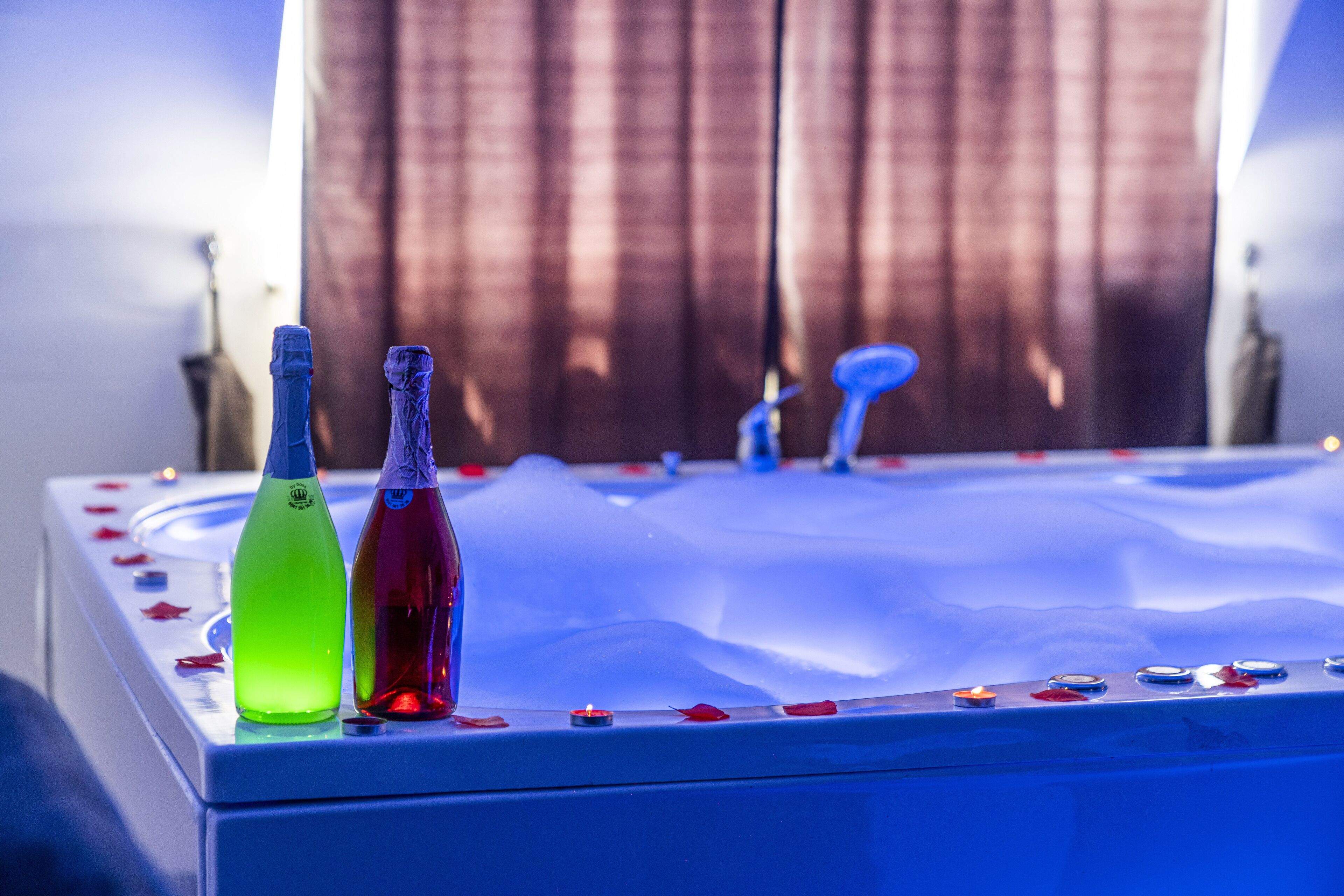 A bathtub with two bottles of liquid, ice, and rose petals.