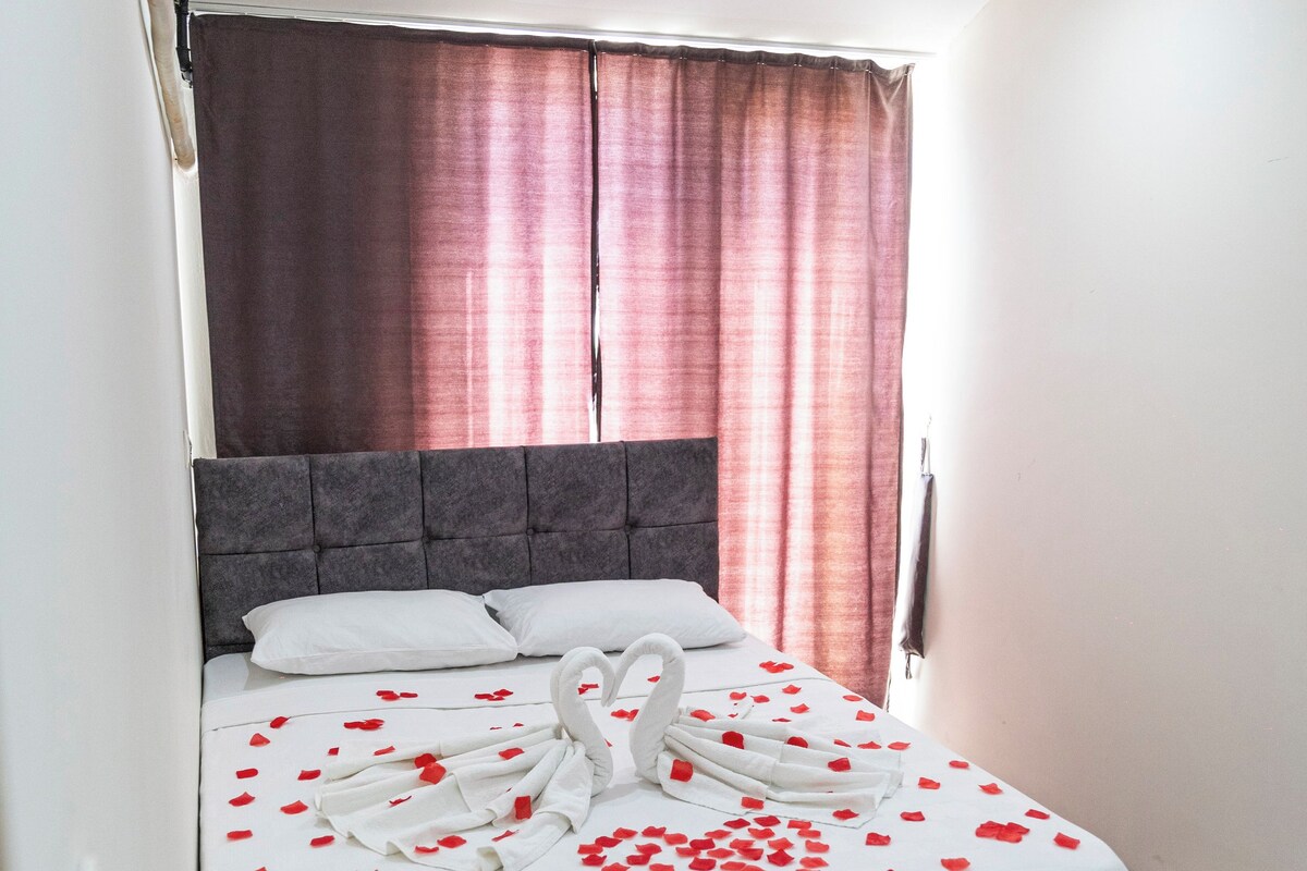 A neatly made bed with a white bedspread, a grey headboard, and a swan-shaped towel arrangement.